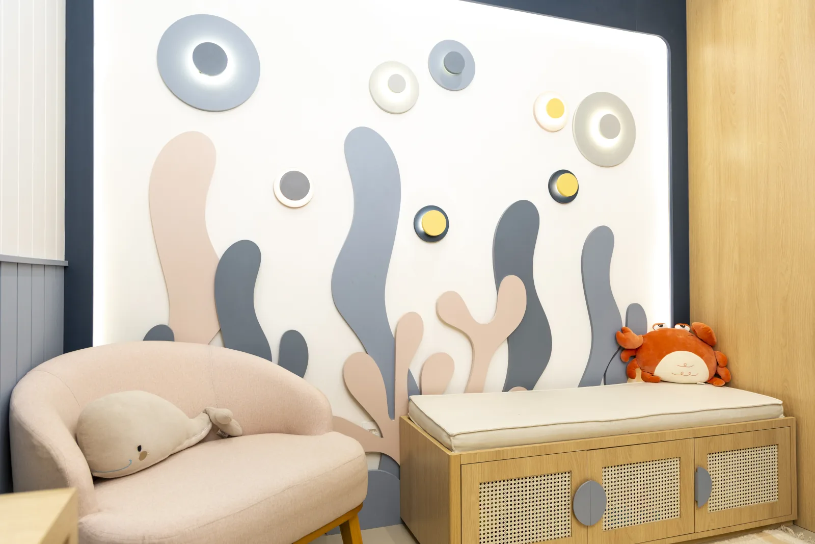 Sala de espera infantil do consultório, com poltrona, parede lúdica temática do fundo do mar e brinquedos.